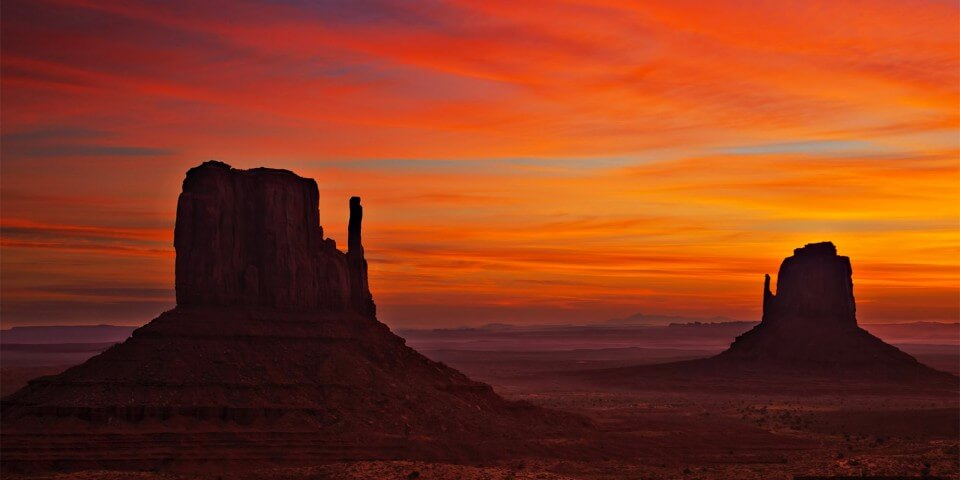 The red sunset makes silhouettes of Monument Valley.