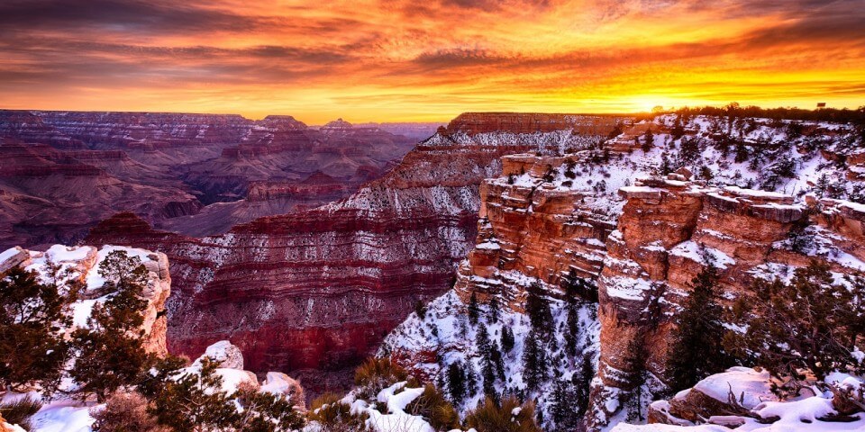 The sun sets above a snowy Grand Canyon.