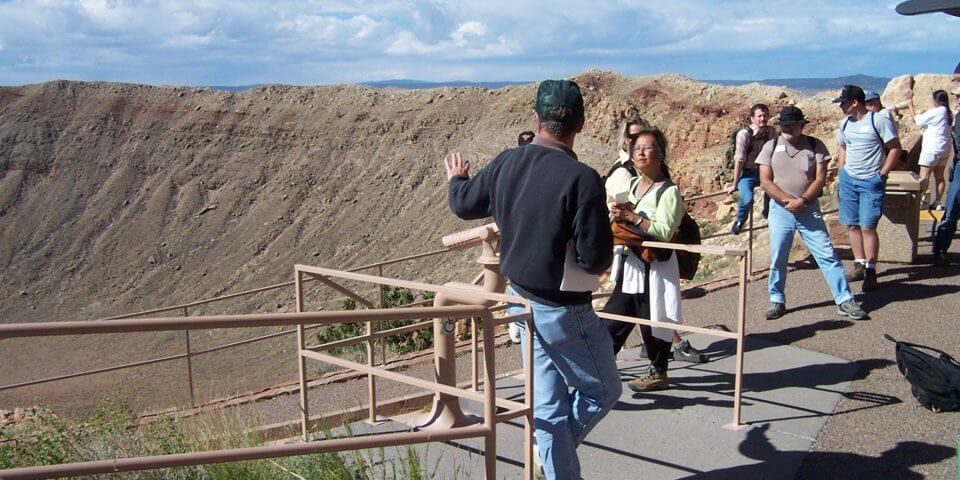 Visitors to the Meteor Crater observe the crater along the rim with telescopes.