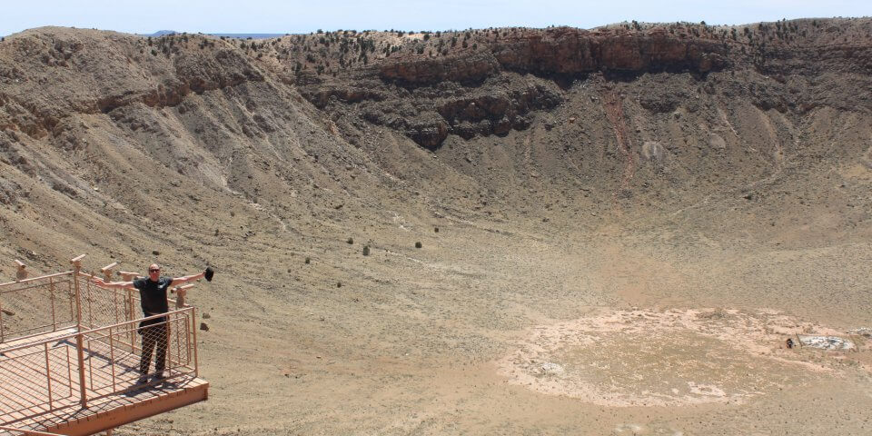 A man stands along the rim of the Meteor Crater in Arizona showing how large the crater is in proportion to his body.