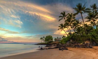 Long exposure photograph of Po'olenalena Beach in Maui, Hawaii, at sunrise, featuring palm trees and rocky shore.