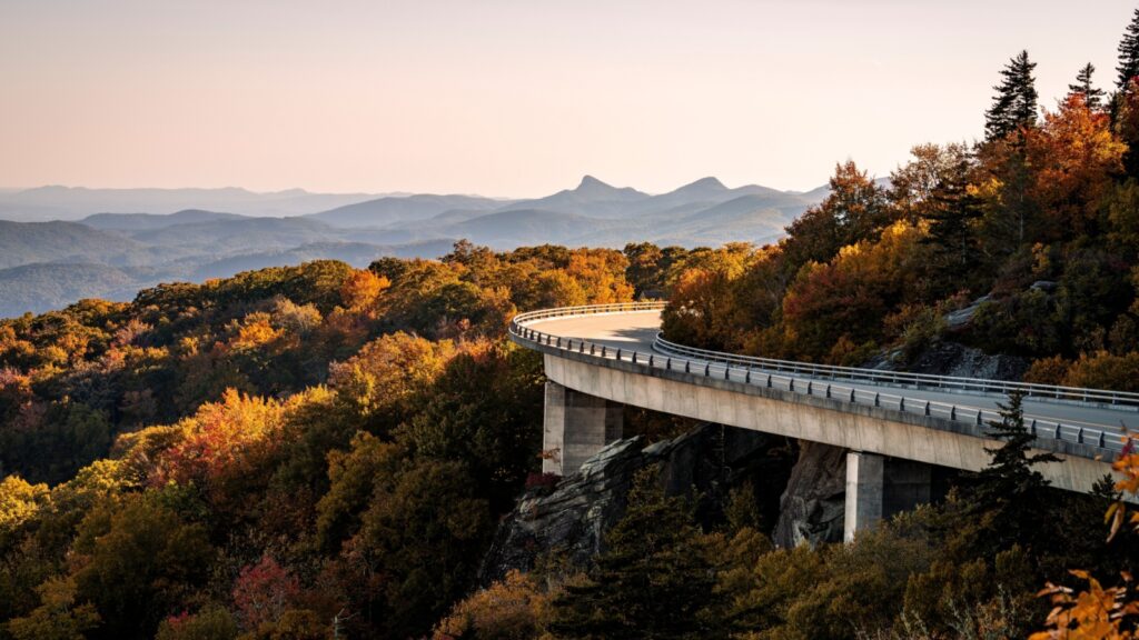 A curved concrete viaduct, the Linn Cove Viaduct, winds through vibrant autumn foliage and mountainous terrain on the Blue Ridge Parkway.