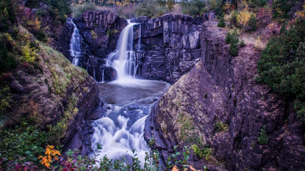 A scenic view of Grand Portage Waterfall surrounded by rocky cliffs and lush greenery.