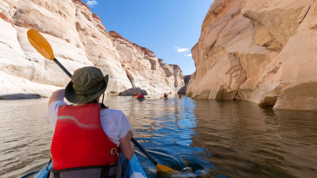 Back of young happy girl kayaking on lake powell with paddle and kayak and life vest on Antelope slot canyon in Arizona during summer.