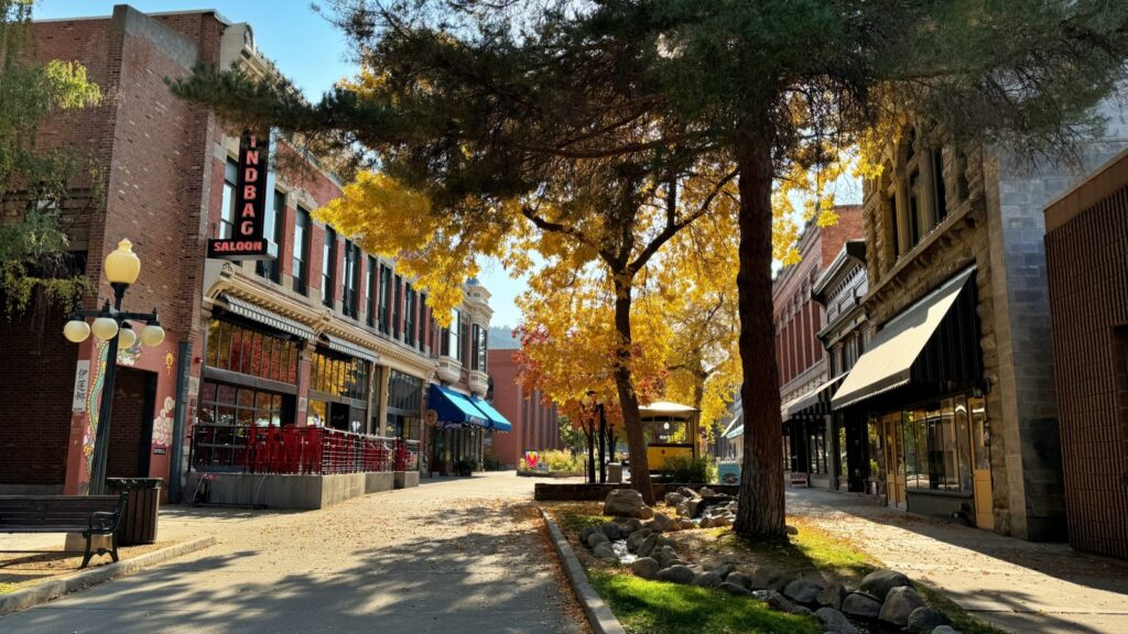 A charming street in Helena, Montana, featuring historic buildings, vibrant autumn trees, and a tranquil stream running alongside the sidewalk.