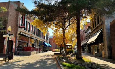 A charming street in Helena, Montana, featuring historic buildings, vibrant autumn trees, and a tranquil stream running alongside the sidewalk.