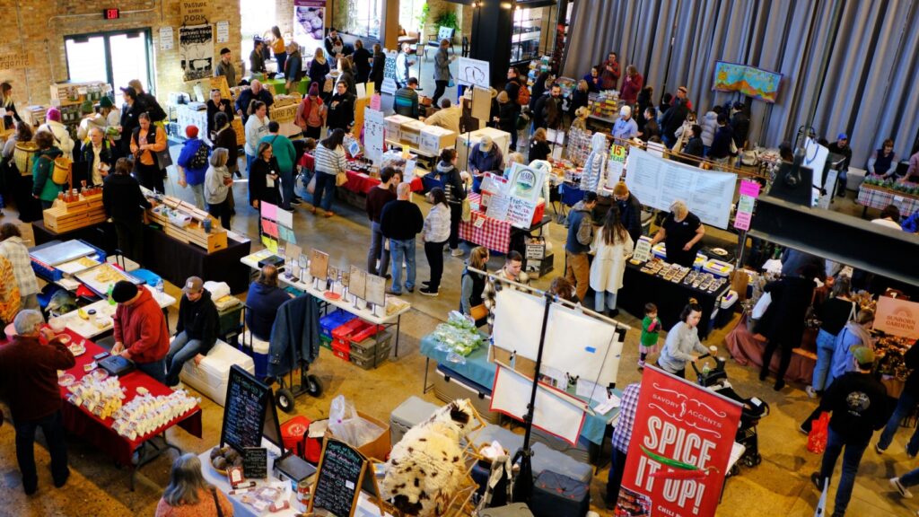 An indoor farmers' market bustling with shoppers and vendors at the Dane County Farmers' Market in Madison, Wisconsin.