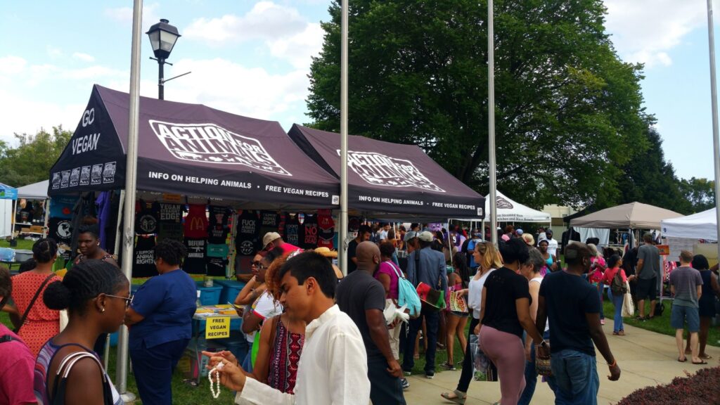 A lively vegan food festival in Baltimore with multiple vendor tents and a large crowd of attendees.