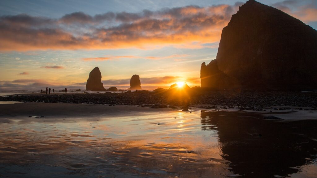 Sunset at Cannon Beach, Oregon, with Haystack Rock and reflections on wet sand.