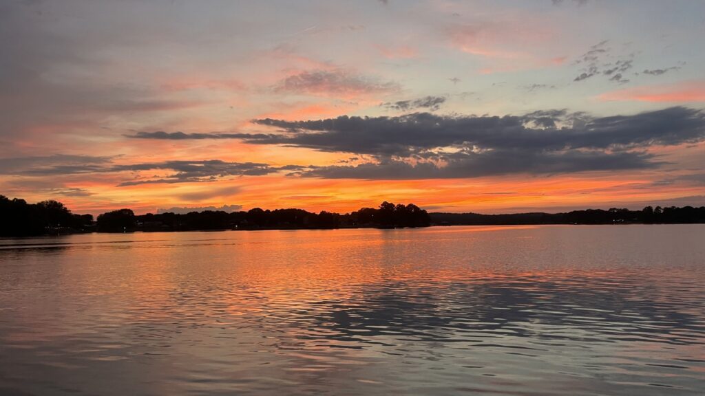 Sunset over a lake, with vibrant orange and pink hues reflected on the water. 

