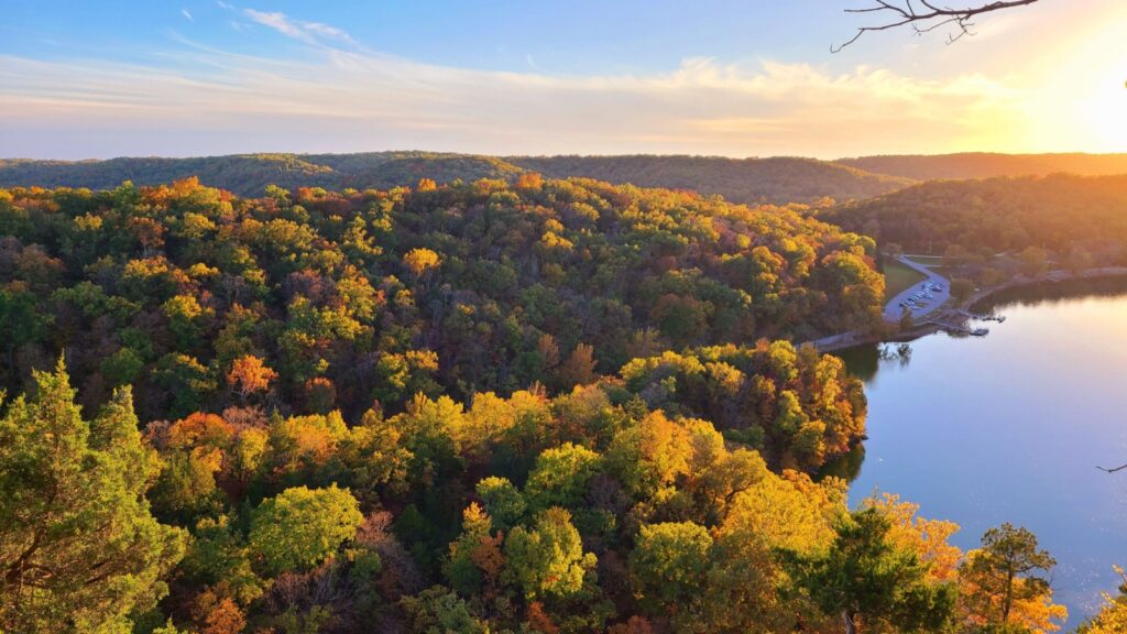 Sunset over a lake surrounded by hills with autumn foliage.
