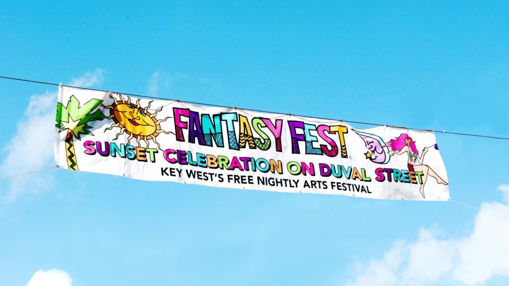 A colorful Key West Fantasy Fest Sunset Celebration banner, hanging against a blue sky with white clouds.