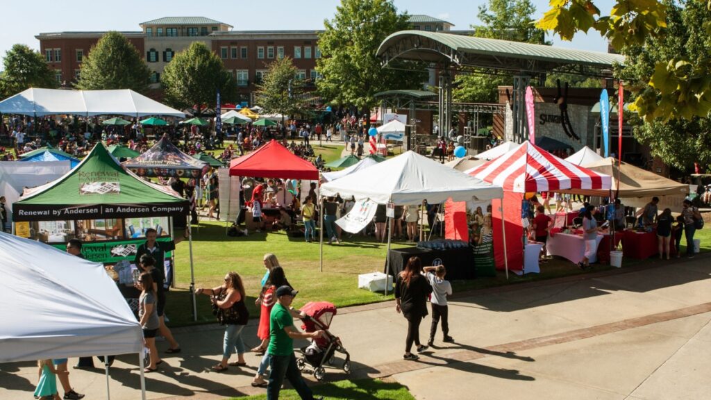 Wide shot of people milling about the vendor tents, displays and games at the Suwanee Fest event