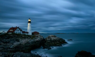 Portland Head Light in Cape Elizabeth, Maine, illuminated at dusk or night with a cloudy sky and rocky coastline.
